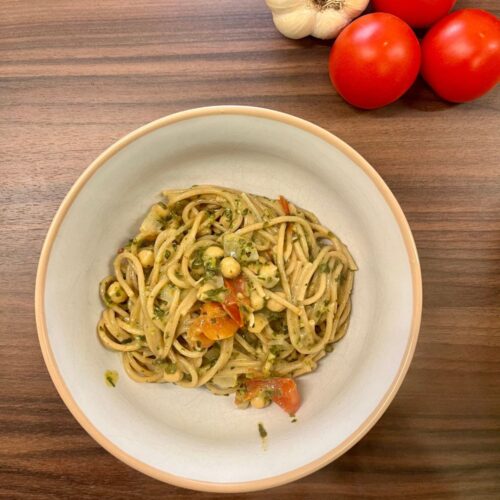 Vegane One Pot Pasta aus dem Ofen in einer Schale angerichtet. Knoblauch und Tomaten im Hintergrund.