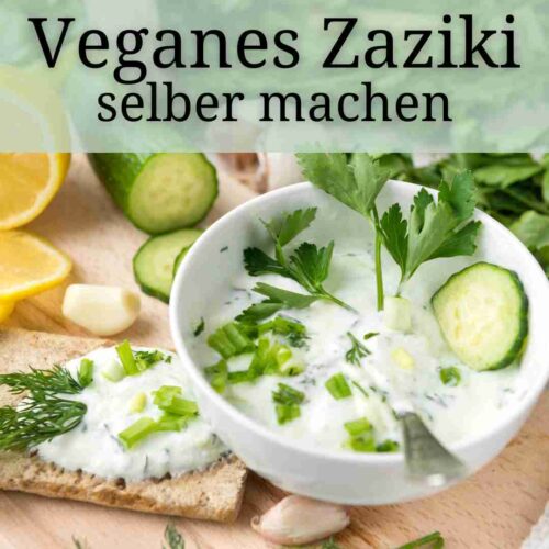 Veganes Zaziki angerichtet in einer weissen Schale, dekoriert mit Gurke, Kraeutern und Knoblauch.