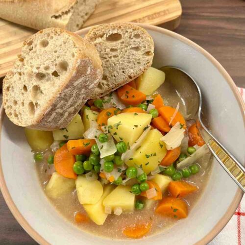 Kartoffeleintopf mit Weisswein, serviert mit Baguette. In der Suppe sind ausserdem Erbsen, Karotten und Weisskohl, dekoriert mit Kraeutern.
