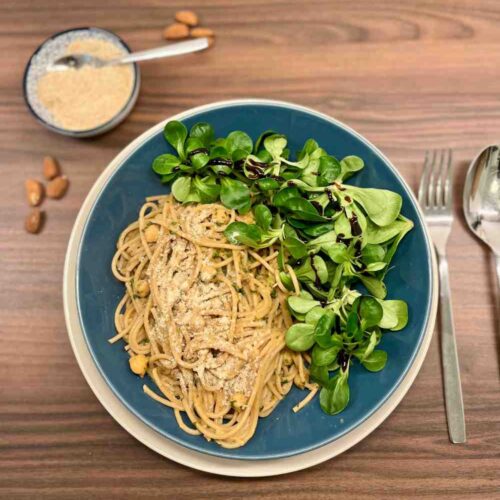 Mandelpasta mit Spinat und Kichererbsen, angerichtet mit Feldsalat und Balsamico Creme. Im Hintergrund gemahlene Mandeln.