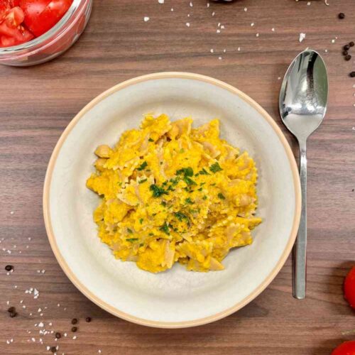 Nudeln mit Curry Kokos Sauce aus Karotten mit Kichererbsen und frischen Tomaten. Dekoriert mit Kraeutern und gemahlenem Pfeffer.